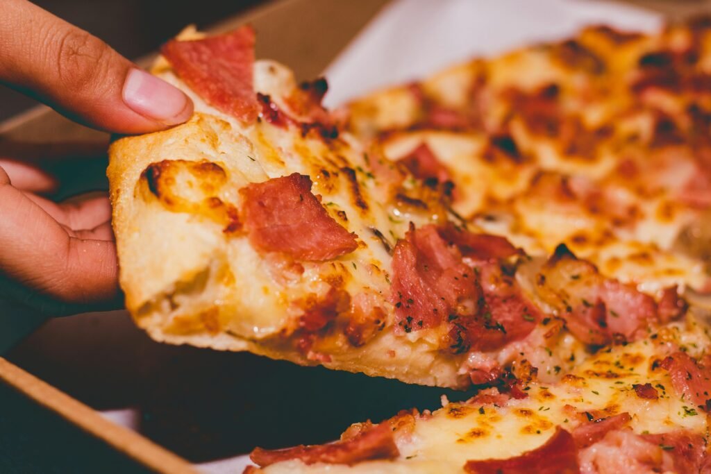 pexels-photo-1653877-1653877 Close-up of a hand holding a delicious slice of pepperoni pizza.